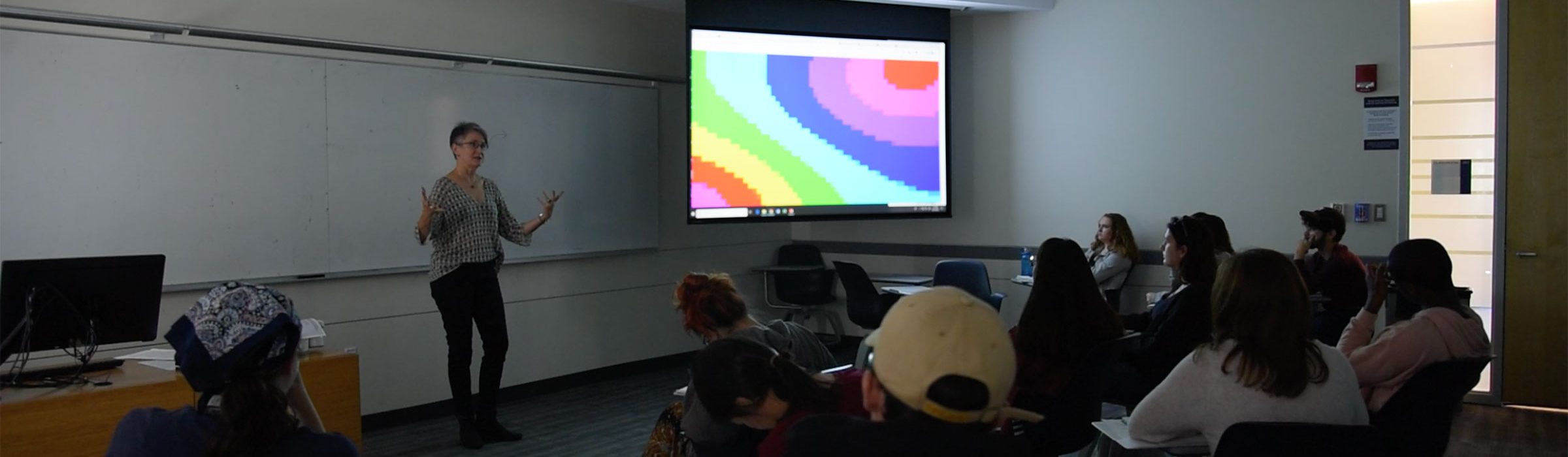 teacher in front of classroom with students and digital art image onscreen